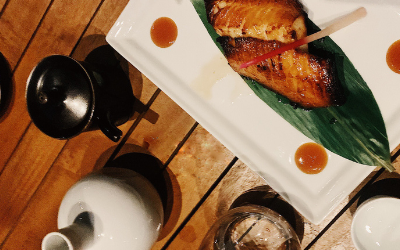 A plate of miso-glazed cod set on a banana leaf next to a bottle of sake.