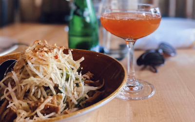 My meal from Haisous featured a bowl of papaya salad with tofu on top, a green glass bottle of sparkling water, and an orange mezcal cocktail in a cocktail glass.